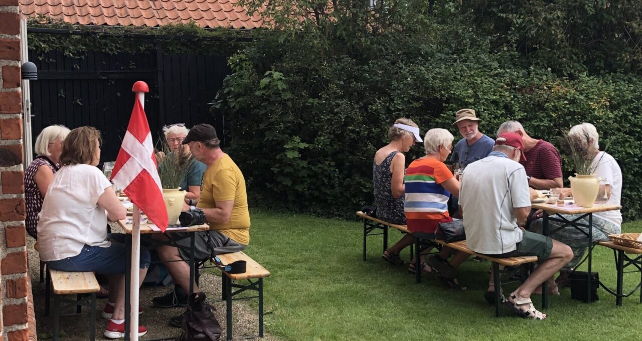 Folk sidder i Vores Marsks have på bænke under et 4+ Tønder Festival arrangement